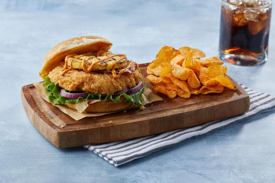 sweet and spicy chicken sandwich with chips and a drink