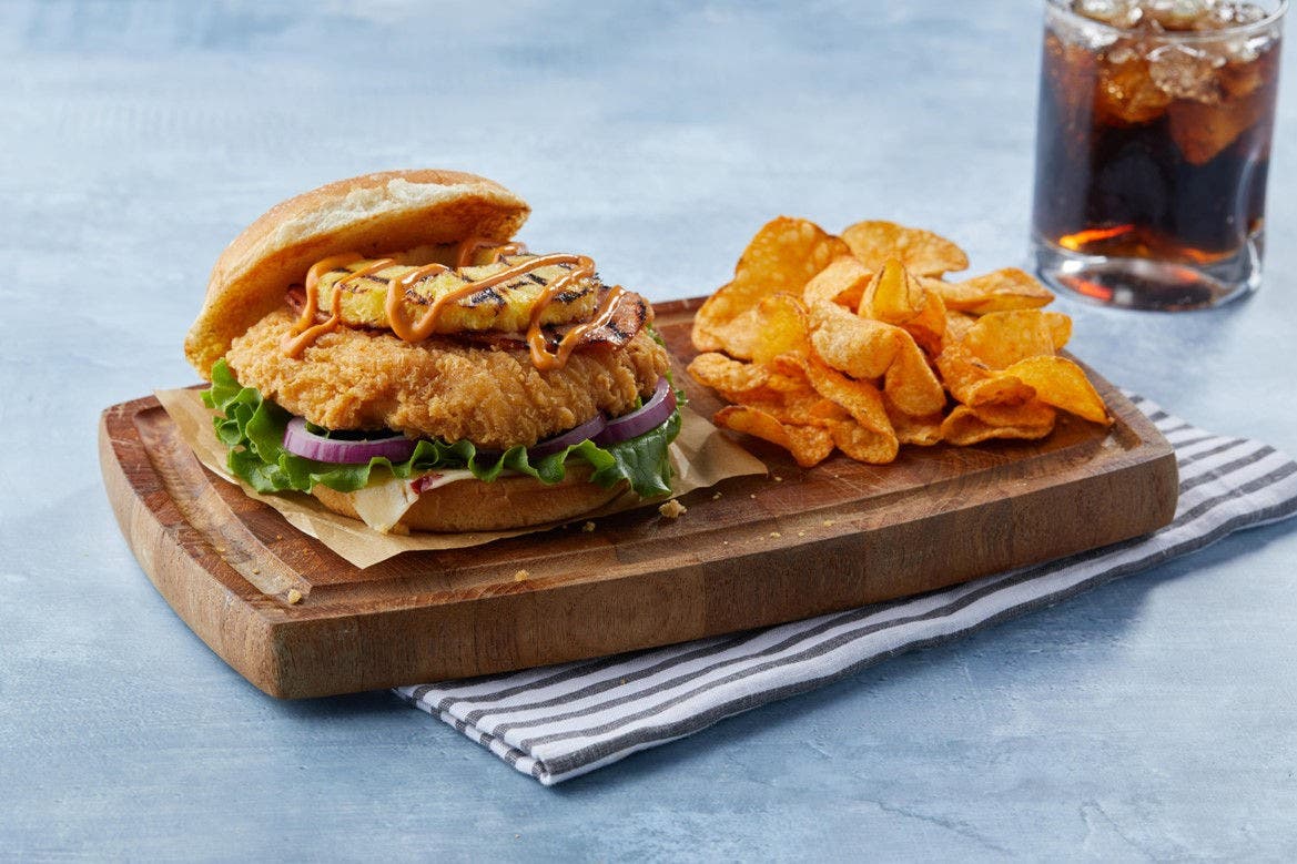 sweet and spicy chicken sandwich with chips and a drink
