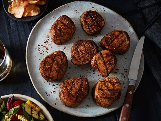 Spiced and grilled pork tenderloin medallions on a plate next to a drink.
