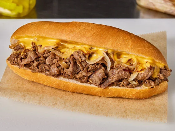Beef Steak on a hoagie roll with onions and cheese sauce, on parchment paper