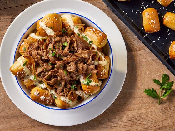 Plated bowl with pretzels, beef slices and white aioli sauce