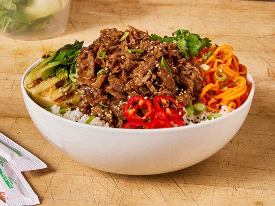Beef steak bowl with cilantro, carrots, red peppers and bok choy, served over rice on a white bowl. 