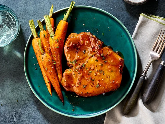 Pork porterhouse steak coated in hot honey and garlic glaze, paired with cooked baby carrots.