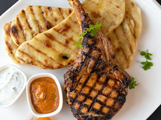 Grilled pork tomahawk on plate with sauces, tomatoes and onions.