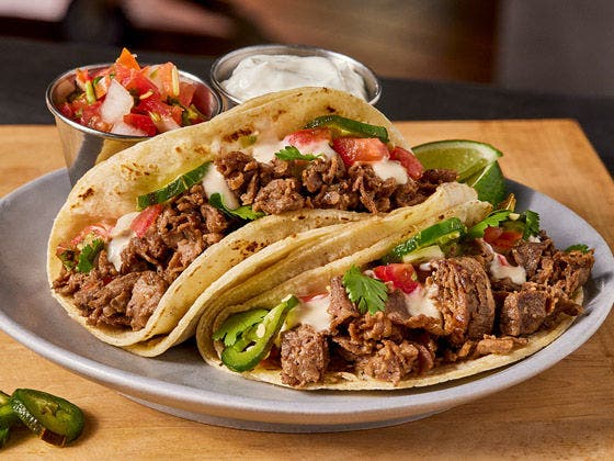 Two plated carne asada soft tacos with pico and sour cream