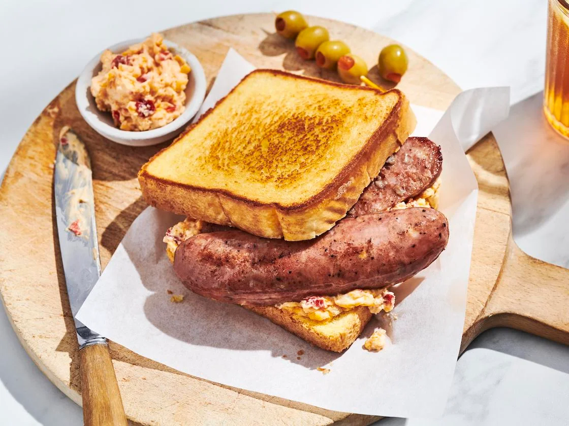 Grilled sausage sandwich with pimento cheese on Texas toast, served on a wooden board