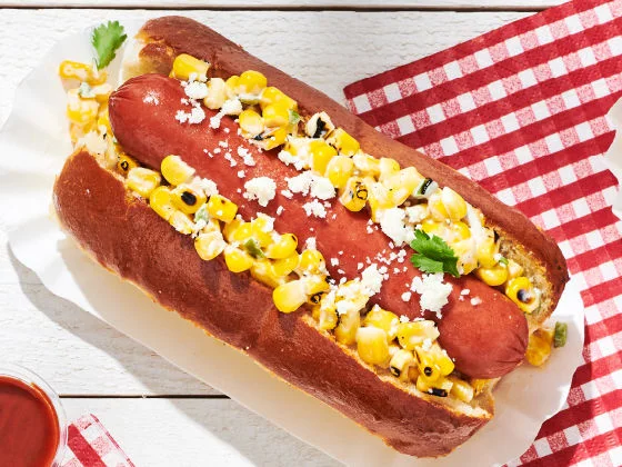 Mexican elote corn dog with corn salad, cotija cheese, and cilantro in a toasted bun on a white tray