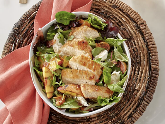 Grilled Chicken and grilled peach wedges are placed on a bed of a fresh arugula and spring mix