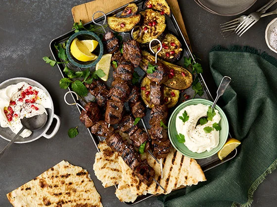 Grilled pomegranate steak tip kebabs paired with grilled flatbread, za'atar roasted eggplant, whipped garlic toum and fresh lemon wedges
