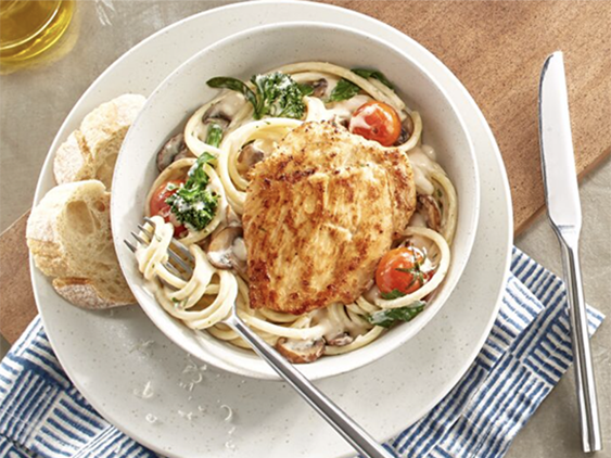 Chicken Breast is placed on a bed of tender bucatini pasta, topped with cherry tomatoes and broccolini