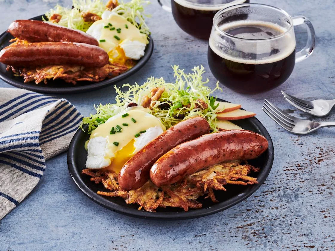 Brunch with sausages, poached eggs on latkes, and salad on a blue-gray table